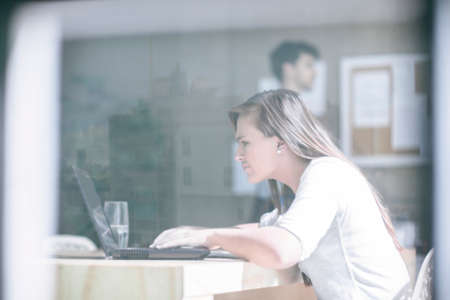 Window view of female designer working on laptop at design studioの写真素材
