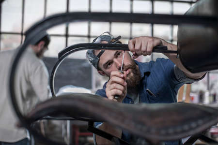 Young craftsman using screwdriver on chair in antique restoration workshopの写真素材