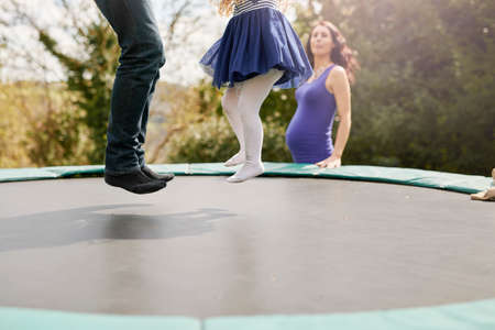 Low section of father and daughter bouncing on trampolineの写真素材