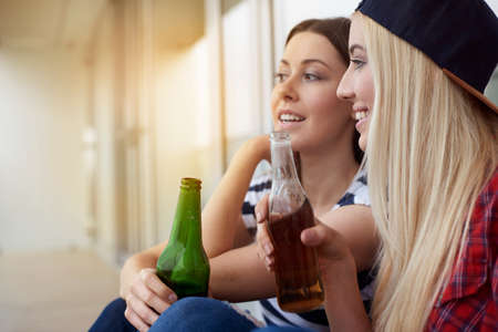 Two female friends, sitting outdoors, drinking bottled beerの写真素材