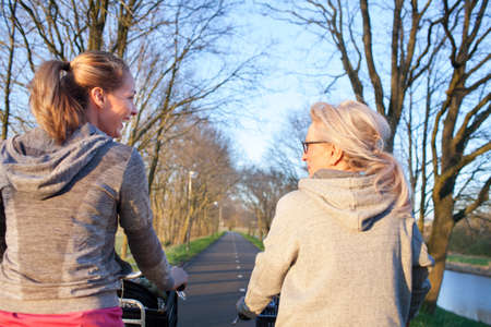 Rear view of women face to face cycling on tree lined roadの写真素材