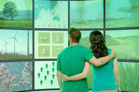 Young couple arms around each other, standing in front of graphical screens, displaying...
