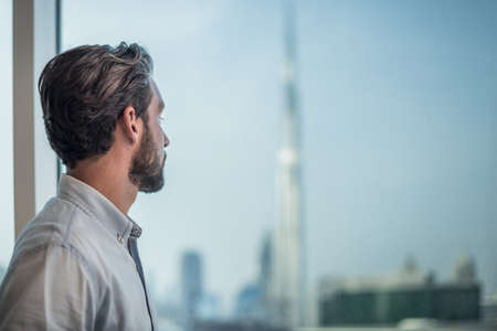 Businessman gazing through window with city view, Dubai, United Arab Emiratesの写真素材
