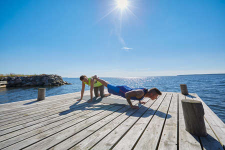 Man on pier doing press ups, legs raised on friendの写真素材