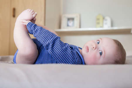 Baby boy lying on bed playing with his feet