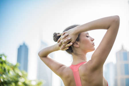 Woman training, eyes closed with hands behind head in park, Dubai, United Arab Emiratesの写真素材