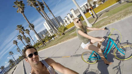 Man taking selfie cycling with girlfriend at Venice Beach, California, USA