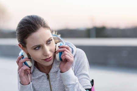 Young woman, outdoors, putting on headphones, looking away