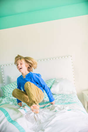 Boy jumping on bed smilingの写真素材