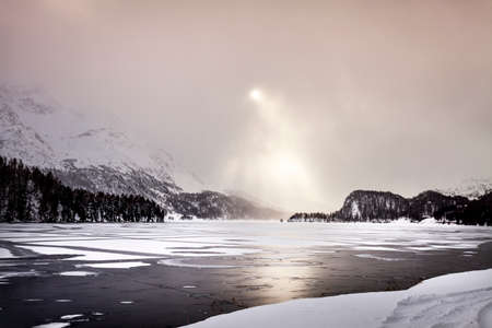 Sunbeams shining on frozen lake and snow covered mountains, Engadin, Switzerland