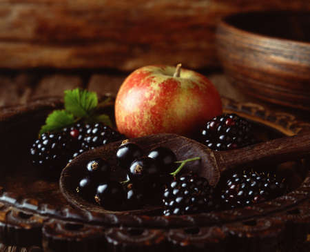 Apple, blackberries and blackcurrants in vintage wooden bowl with wooden spoon, close-upの写真素材