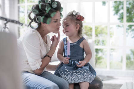 Mother in hair rollers pointing cheek to daughterの写真素材