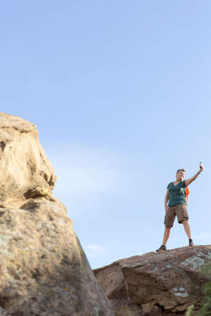 Woman hiker standing on top of rocks using smartphone to take selfieの写真素材