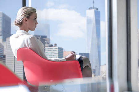 Young businesswoman sitting in front of New York skyline window, USAの写真素材