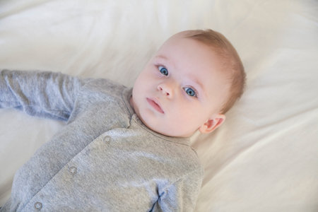 Overhead portrait of blue eyed baby boy lying on bed