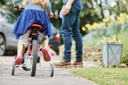Father teaching daughter to ride bicycle on streetの写真素材
