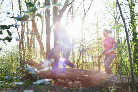 Women in forest jumping over fallen treeの写真素材