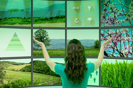 Young woman standing in front of graphical screens, displaying environmental images, rear viewの写真素材