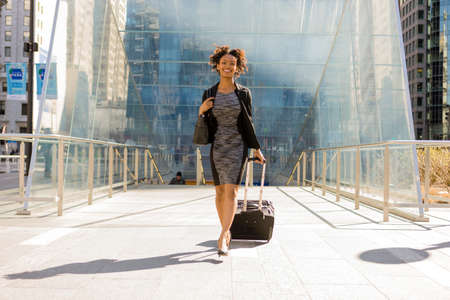 Businesswoman walking outdoors, pulling wheeled suitcaseの写真素材