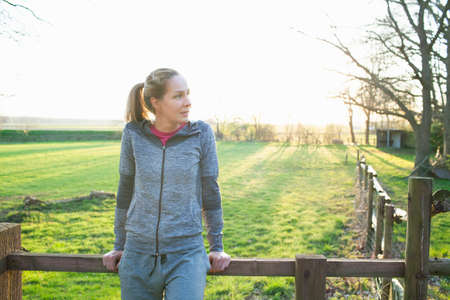Woman wearing sports clothing leaning against fence looking awayの写真素材