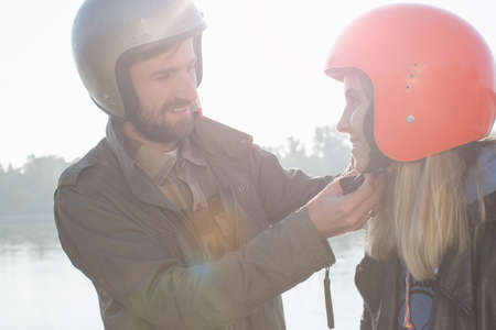 Man helping woman put on crash helmet, smilingの写真素材