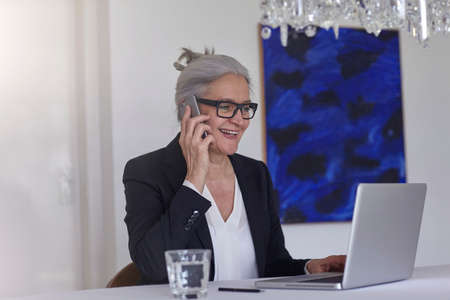 Woman using laptop making telephone call on smartphoneの写真素材