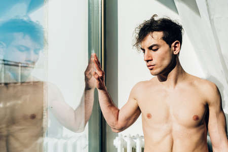 Bare chested man looking out of windowの写真素材