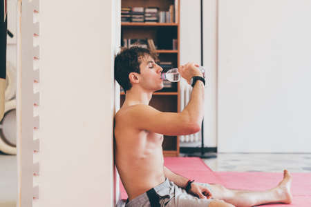 Side view of man leaning against column drinking water from bottleの写真素材