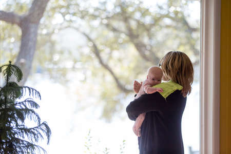 Young woman patting baby daughter in front of window