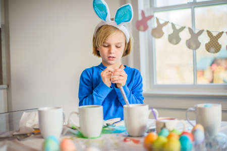 Boy at table wearing bunny ears decorating eggs for Easter