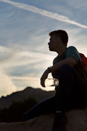 Silhouette of woman hiker sitting holding water bottle looking away
