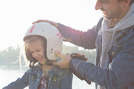 Father putting crash helmet on daughter's head, smilingの写真素材