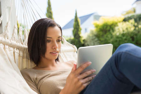 Young woman reclining on garden hammock browsing digital tabletの写真素材