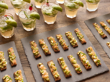 Guacamole, smoked salmon and rye bread canapes with vodka cocktail garnished with lime wedges