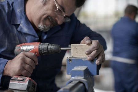 Carpenter drilling wood at workshop bench