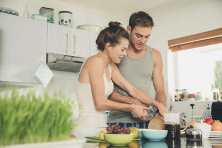 Young woman helping boyfriend to slice wholemeal bread at kitchen counter