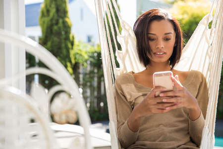 Young woman relaxing on garden hammock reading smartphone texts