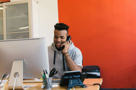 Man at desk in office making telephone call smilingの写真素材