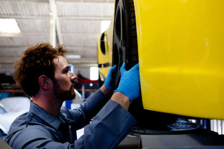 Male mechanic aligning wheel on yellow sports carの写真素材