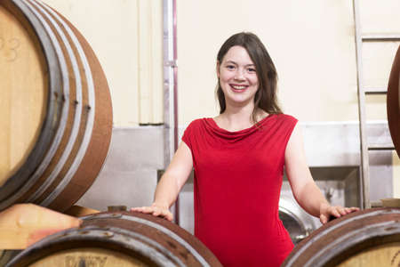 Portrait of young woman in wine cellar, beside wine barrels, smiling