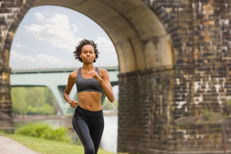 Woman wearing spandex jogging by bridge