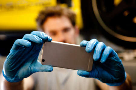 Male mechanic in workshop taking photo of car with mobile phoneの写真素材