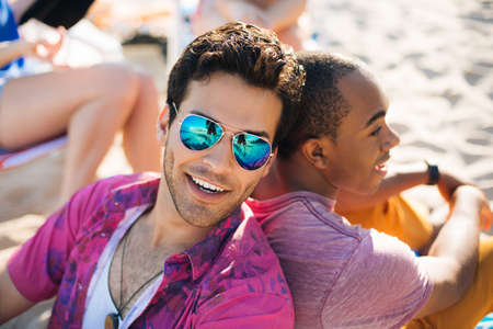 Portrait of two men sitting back to back on beach, Santa Monica, California, USA