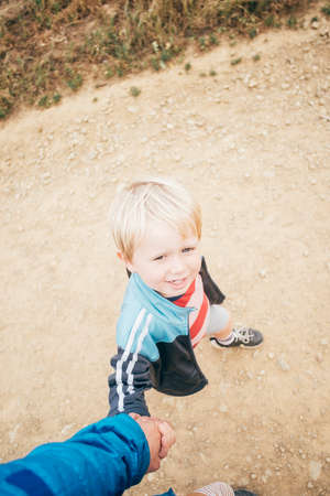Over shoulder view of boy holding brothers hand on dirt track