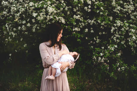 Mid adult woman carrying baby daughter in arms by garden apple blossomの写真素材