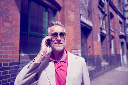 Mature man walking along street, using smartphoneの写真素材