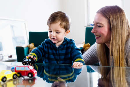 Mid adult woman and baby son playing with toy cars on table