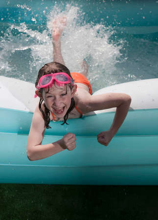 Portrait of girl lying on front splashing water in paddling poolの写真素材
