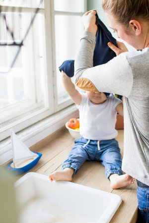 Woman undressing baby son at kitchen sinkの写真素材
