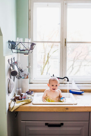 Portrait of baby boy bathing in kitchen sinkの写真素材